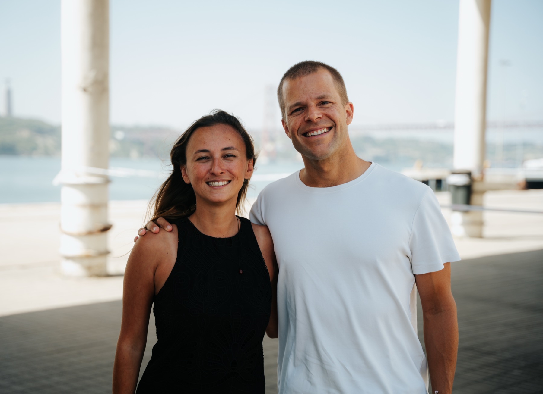 Inês Ribeiro de Brito and Rodrigo Paiva by the river in Lisbon, the 25 de Abril bridge behind them