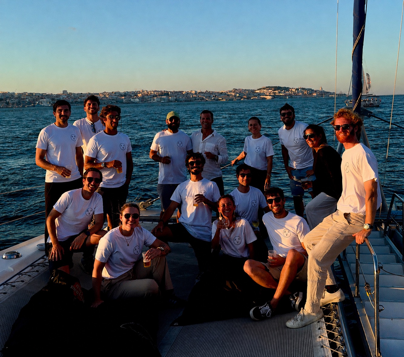 The Atlana team on a sailboat on the Tagus at sunset, Lisbon behind them