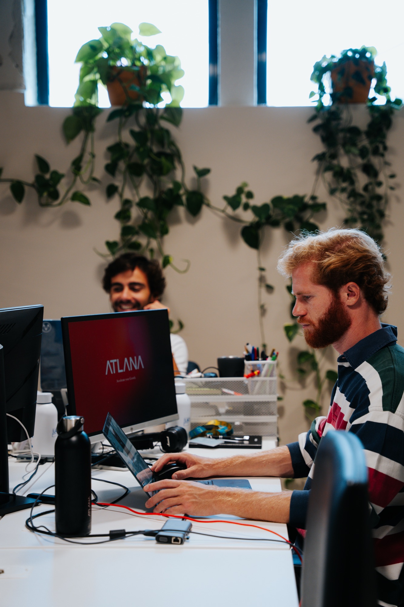 Two Atlana engineers at their desks in the Lisbon office, the Atlana mark on a monitor